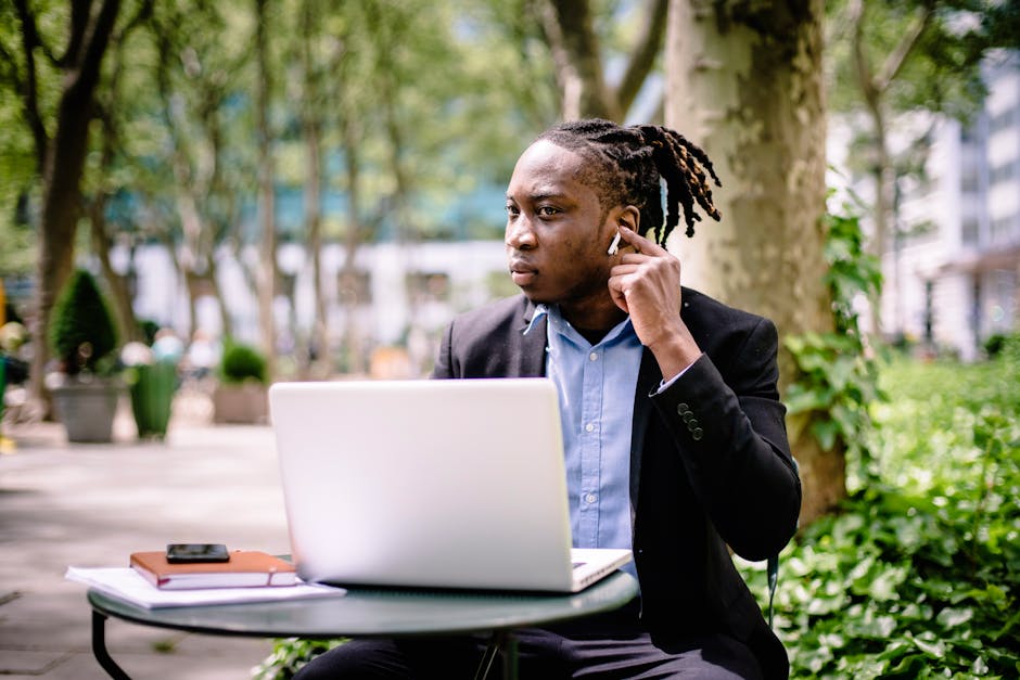 man using wireless earbuds while working on laptop in cafe